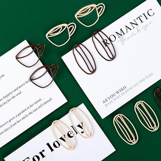 Coffee cup–shaped and oval paper clips arranged on a green background with printed cards.