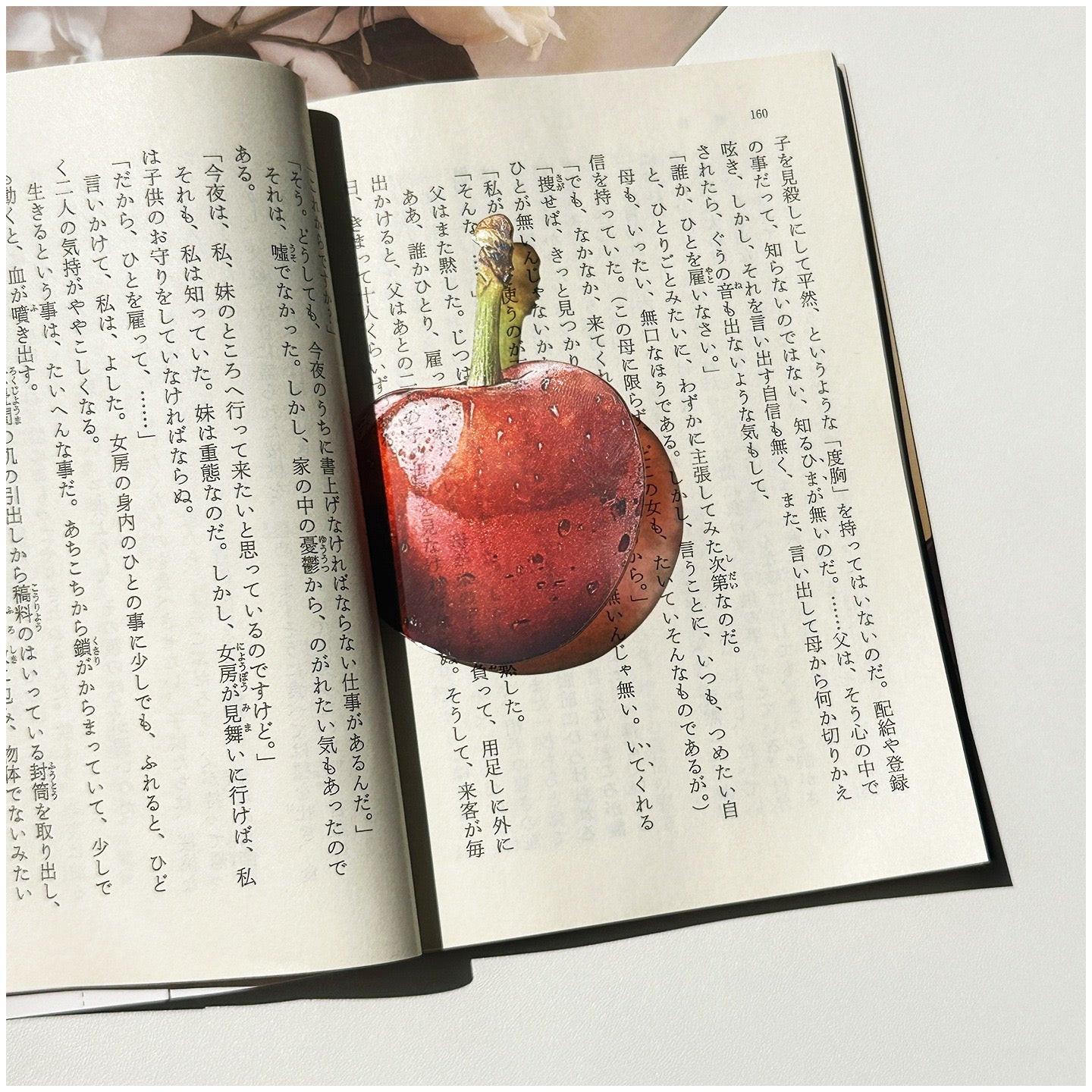 Cherry-shaped transparent bookmark placed inside an open book.