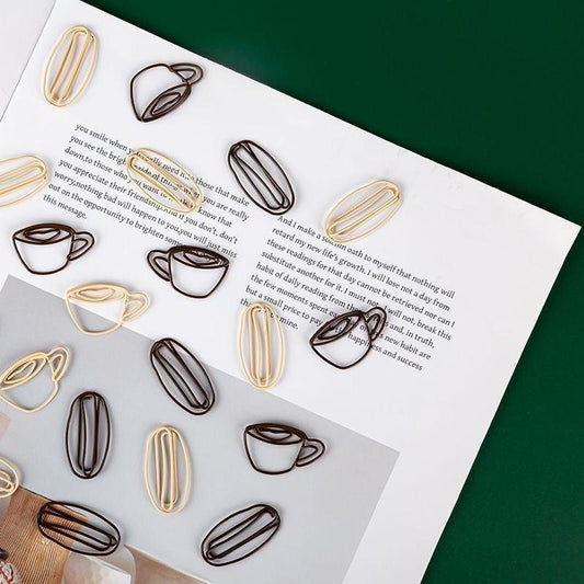 Coffee cup–shaped and oval paper clips scattered across an open book on a green background.
