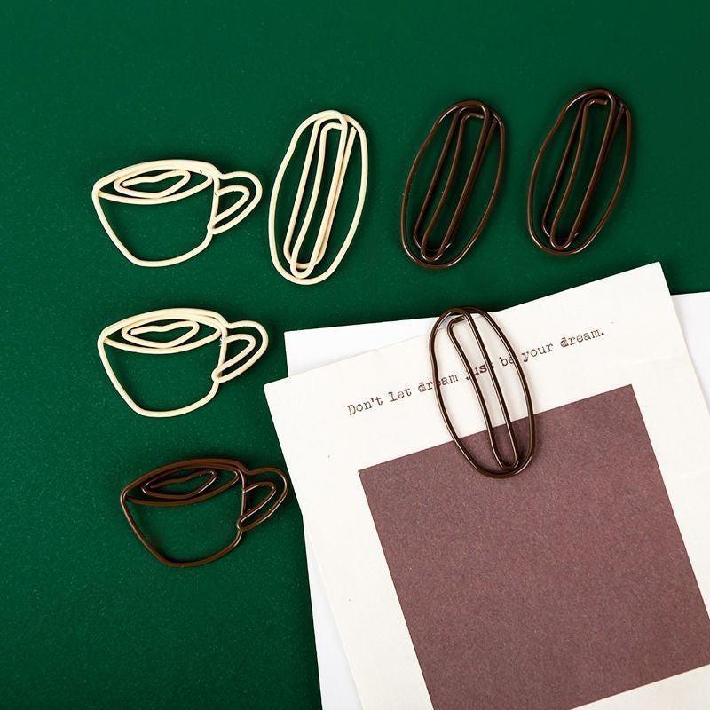 Minimal coffee cup–shaped paper clips displayed on a green background, with one clip holding paper.
