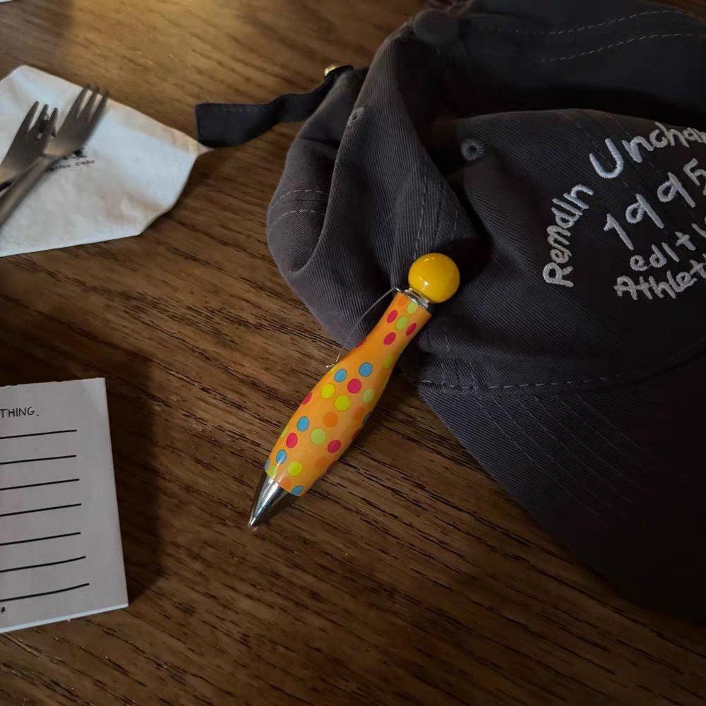 Colorful ballpoint pen placed on a wooden table next to a fabric bag and paper.