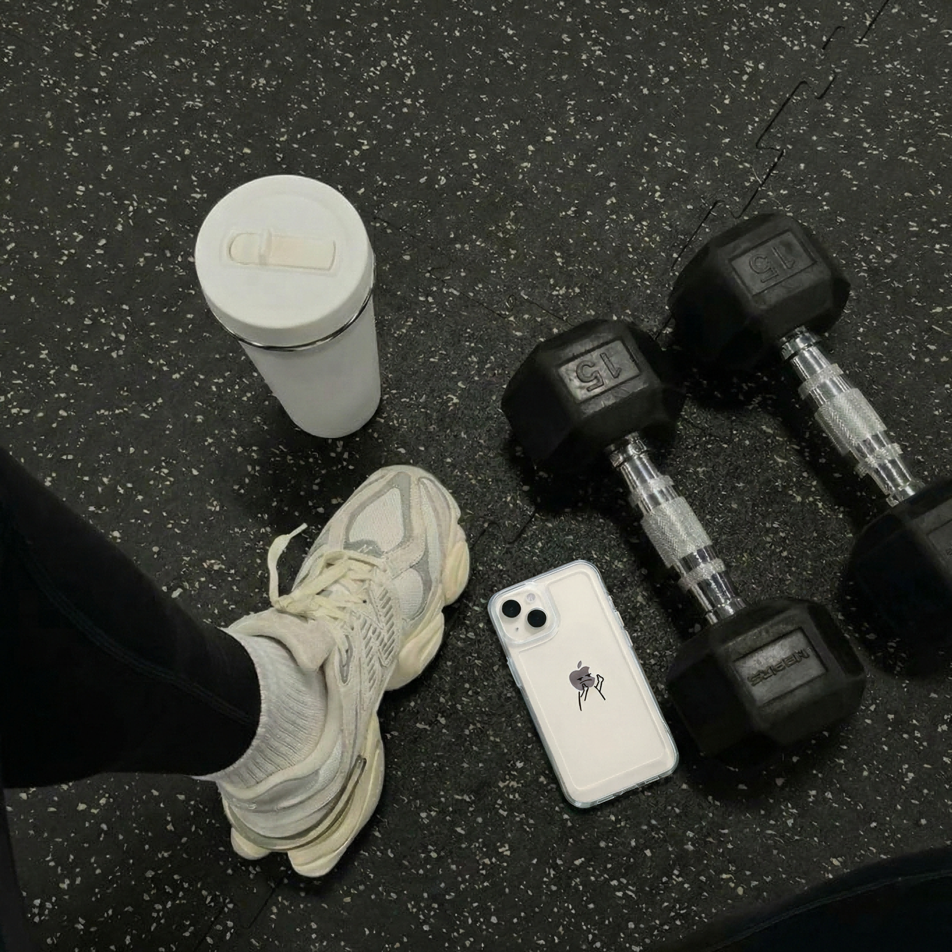 Clear phone case on a gym floor beside dumbbells and sneakers.