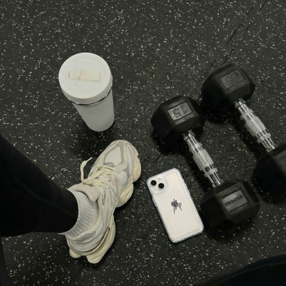 Clear phone case on a gym floor beside dumbbells and sneakers.
