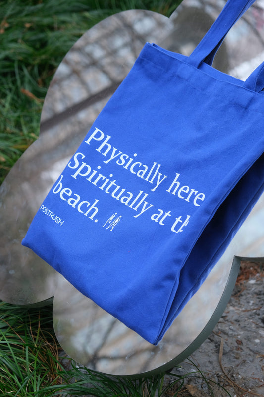 Blue canvas tote bag featuring funny text, photographed outdoors with mirror reflection