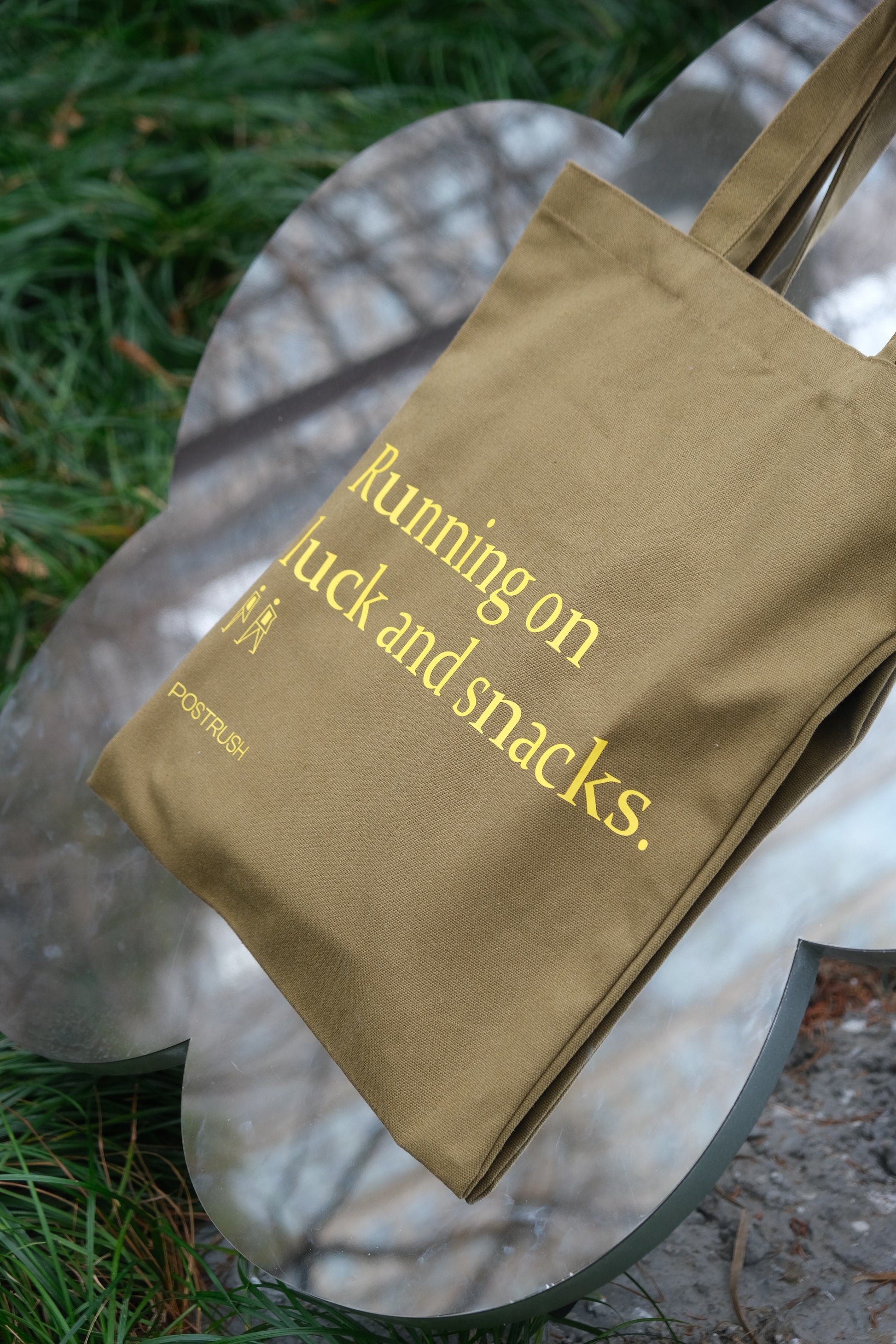 Brown funny tote bag with yellow text on a mirror surface outdoors