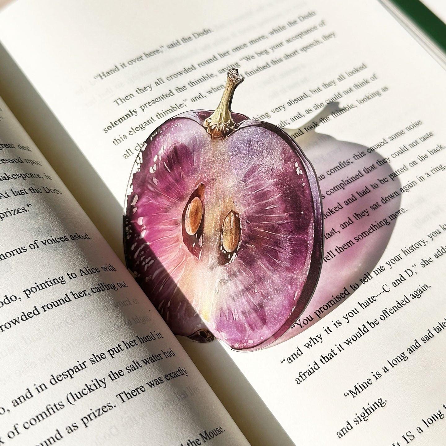 Half grape–shaped transparent bookmark placed inside an open book.