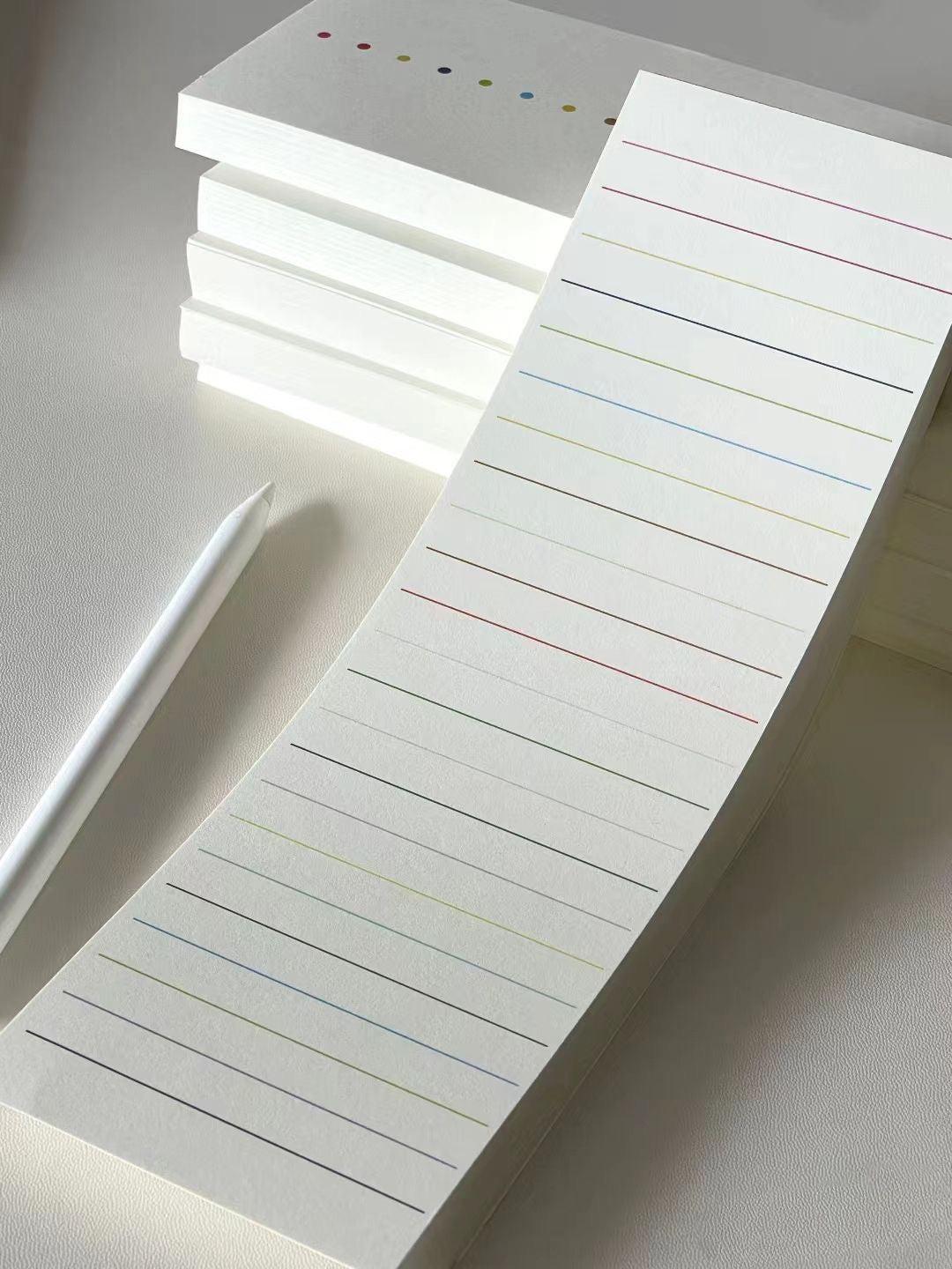 Minimal white lined notepad with subtle multicolored lines, shown in stacked sheets under natural light.