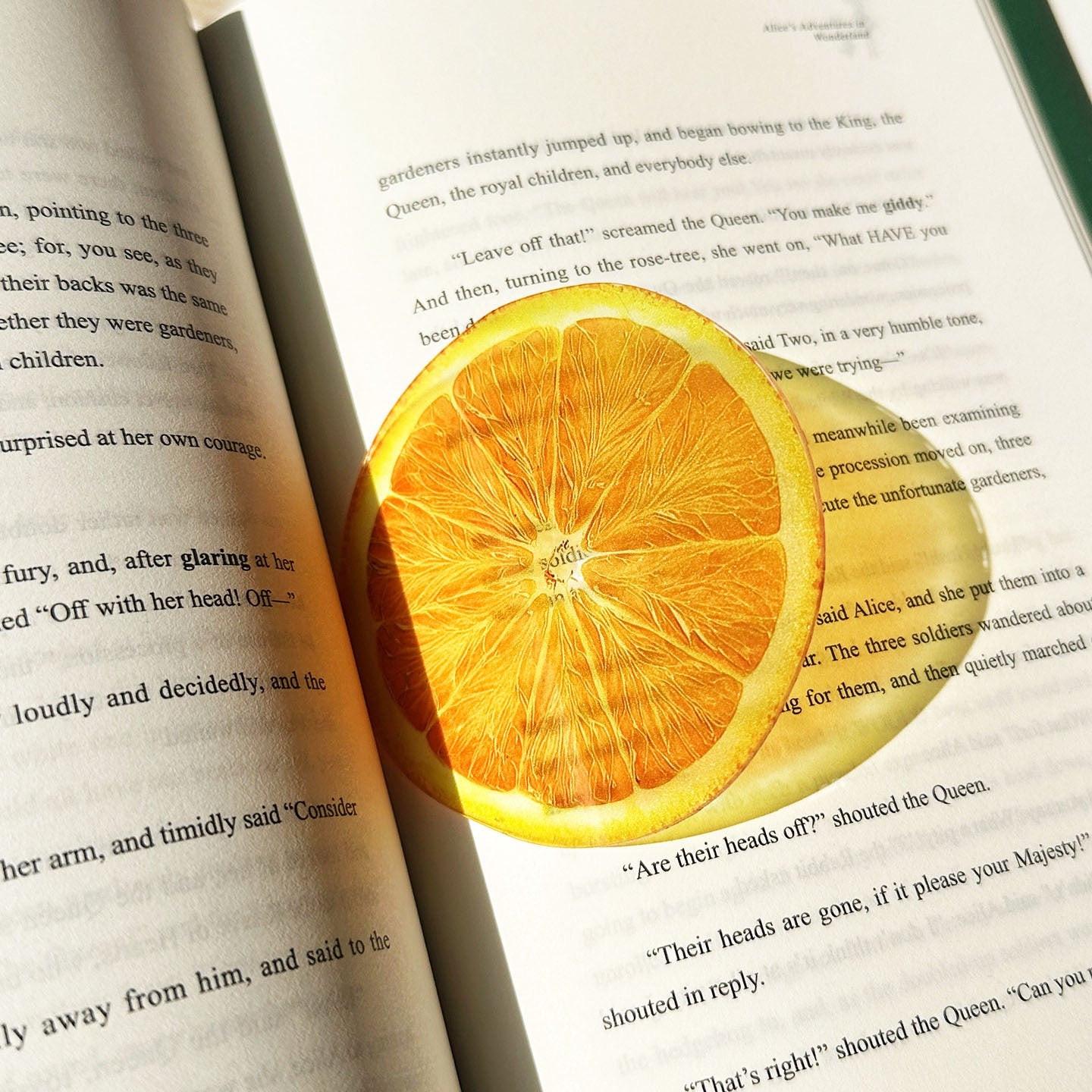 Sliced orange–shaped transparent bookmark placed inside an open book.
