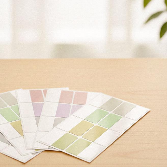 Pastel color label stickers arranged on a wooden desk in a clean, minimal setting.
