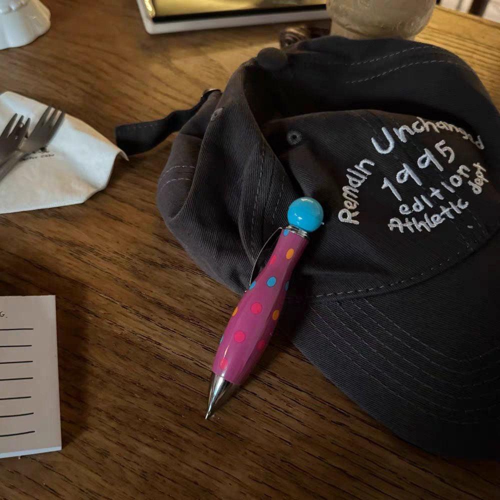 Polka dot ballpoint pen placed on a wooden table next to a fabric bag and paper.