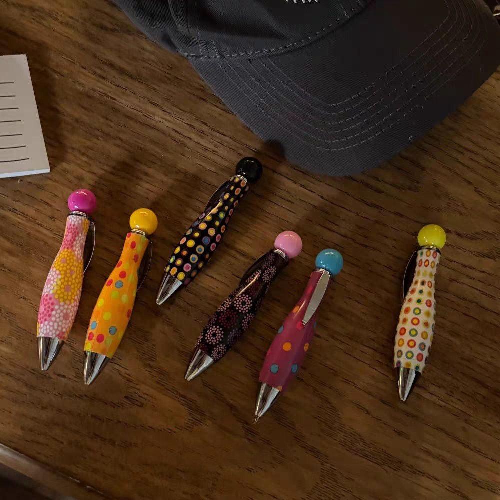 Polka dot ballpoint pens in multiple colorways arranged in a row on a wooden table.