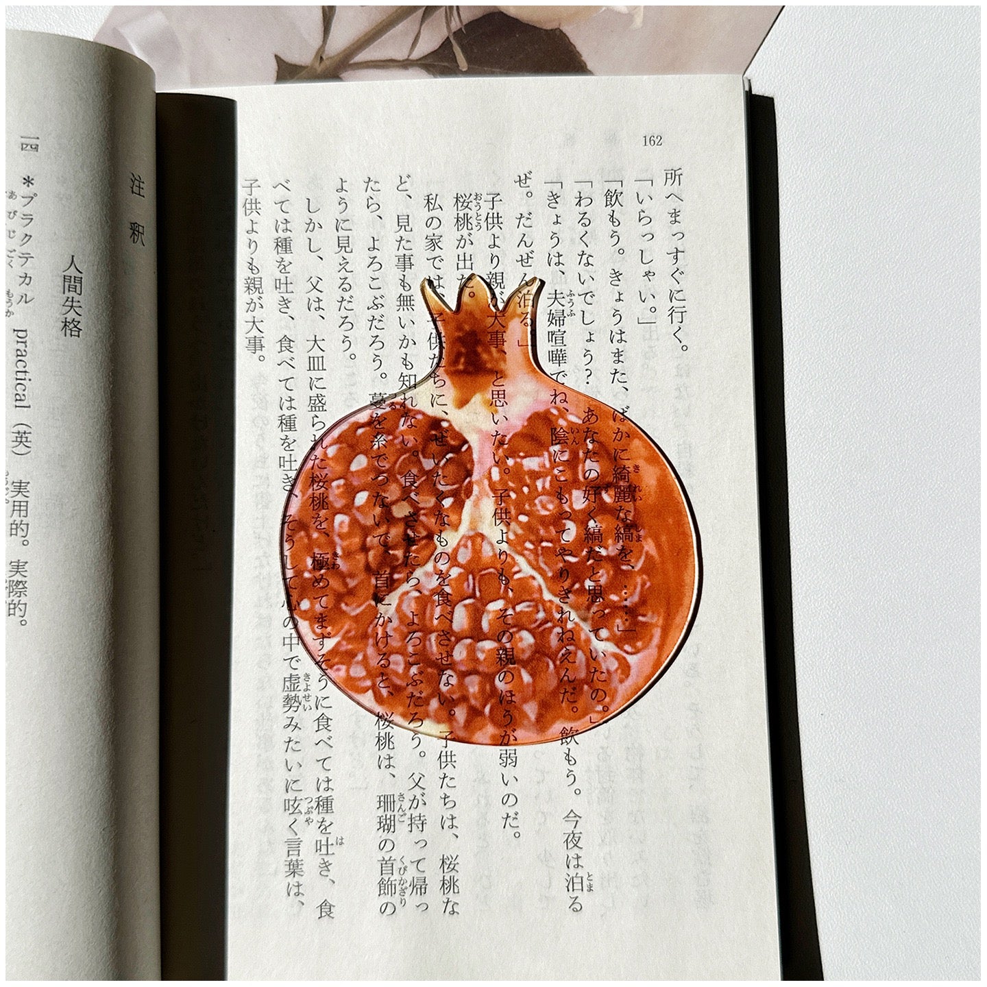 Pomegranate-shaped transparent bookmark placed inside an open book.