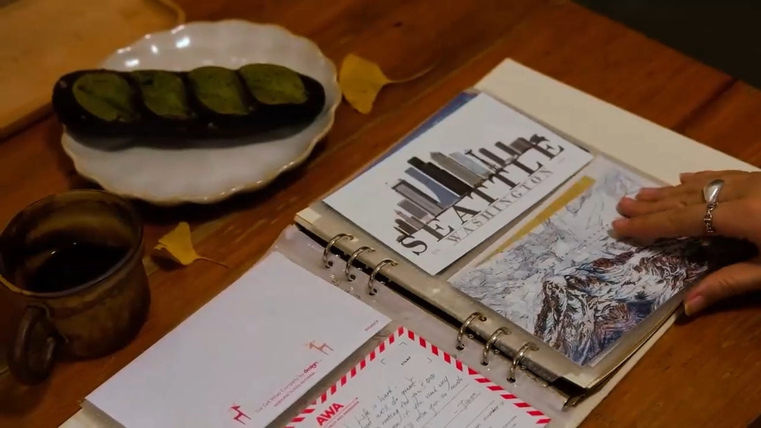 PostRush analog journal postcard album on a coffee shop table, shown in a video of hands flipping through postcard pockets, with short cutaway clips showing the travel memories featured on the postcards.