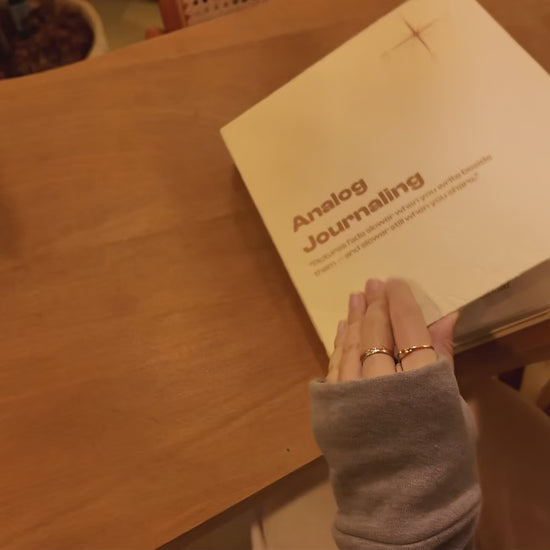 PostRush analog journal postcard album on a coffee shop table, shown in a video of hands flipping through photo pockets, paper pages, and transparent doodle sheets.