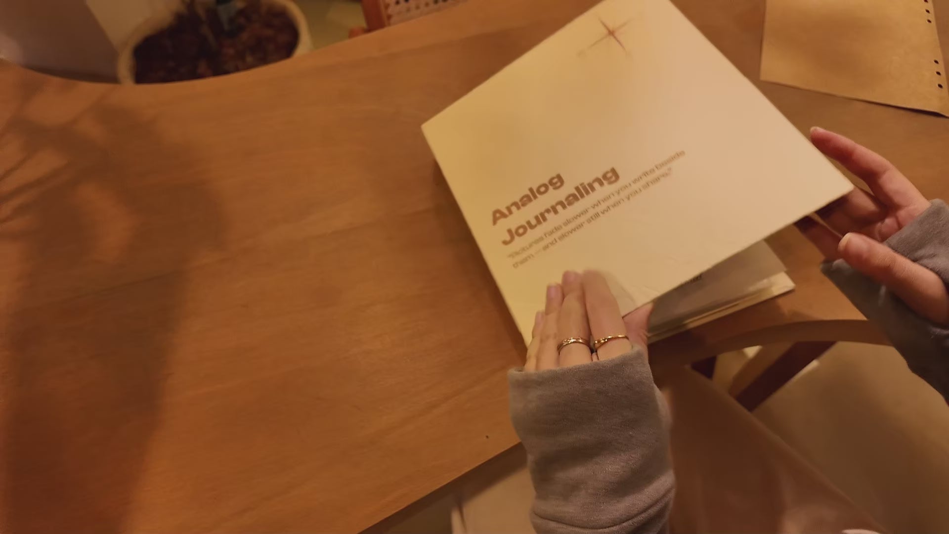 PostRush analog journal postcard album on a coffee shop table, shown in a video of hands flipping through photo pockets, paper pages, and transparent doodle sheets.