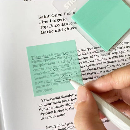 A close-up of annotating a book with green translucent sticky notes and a pen during a quiet reading session.