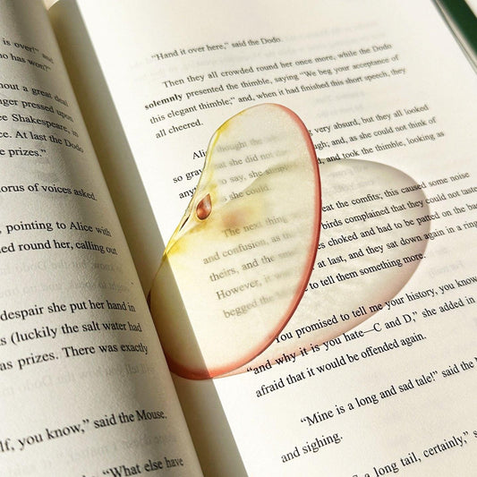 Sliced apple–shaped transparent bookmark placed inside an open book.