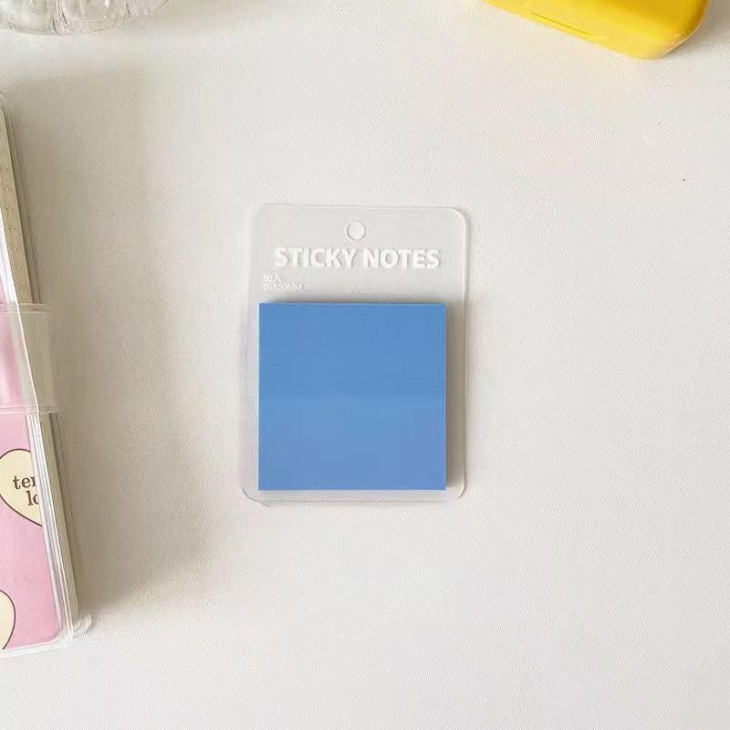 Translucent blue sticky notes placed on a clean white desk in a simple, minimal stationery setup.