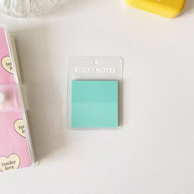 Translucent green sticky notes placed on a clean white desk in a simple, minimal stationery setup.