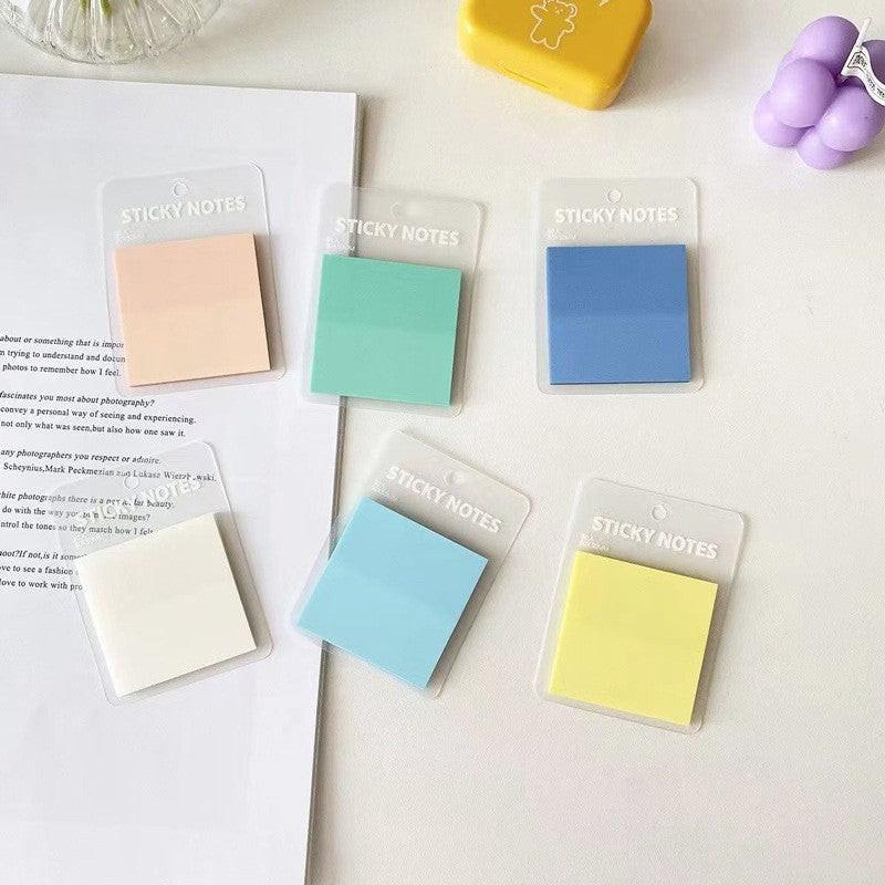 A set of translucent sticky notes in soft pastel colors arranged on a clean white desk.